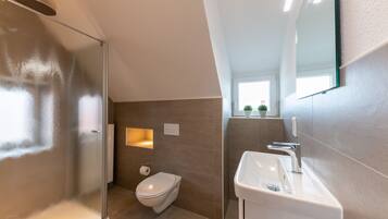 Une salle de bain moderne avec une douche à parois de verre, des toilettes et un lavabo surmonté d’un miroir.