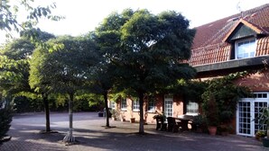A courtyard with a brick pathway, trees, and a building with a tiled roof. - Hotel Leppiner Hof (Arendsee)