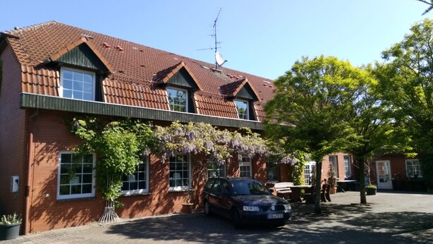 A two-story brick building with a tiled roof, a parked car, and a tree with green leaves. - Hotel Leppiner Hof (Arendsee)