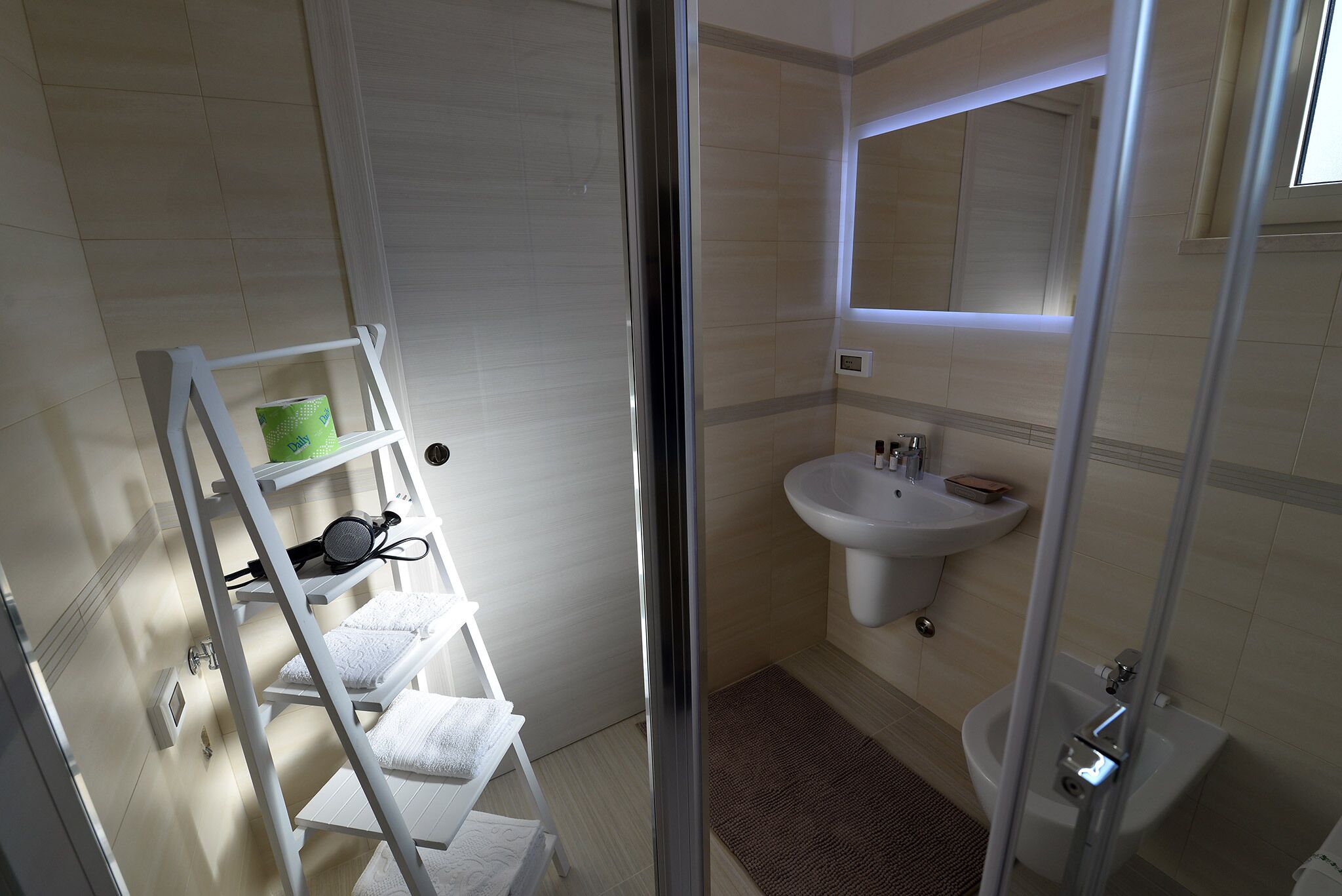 Un baño con lavamanos blanco, espejo y toallero con toallas.