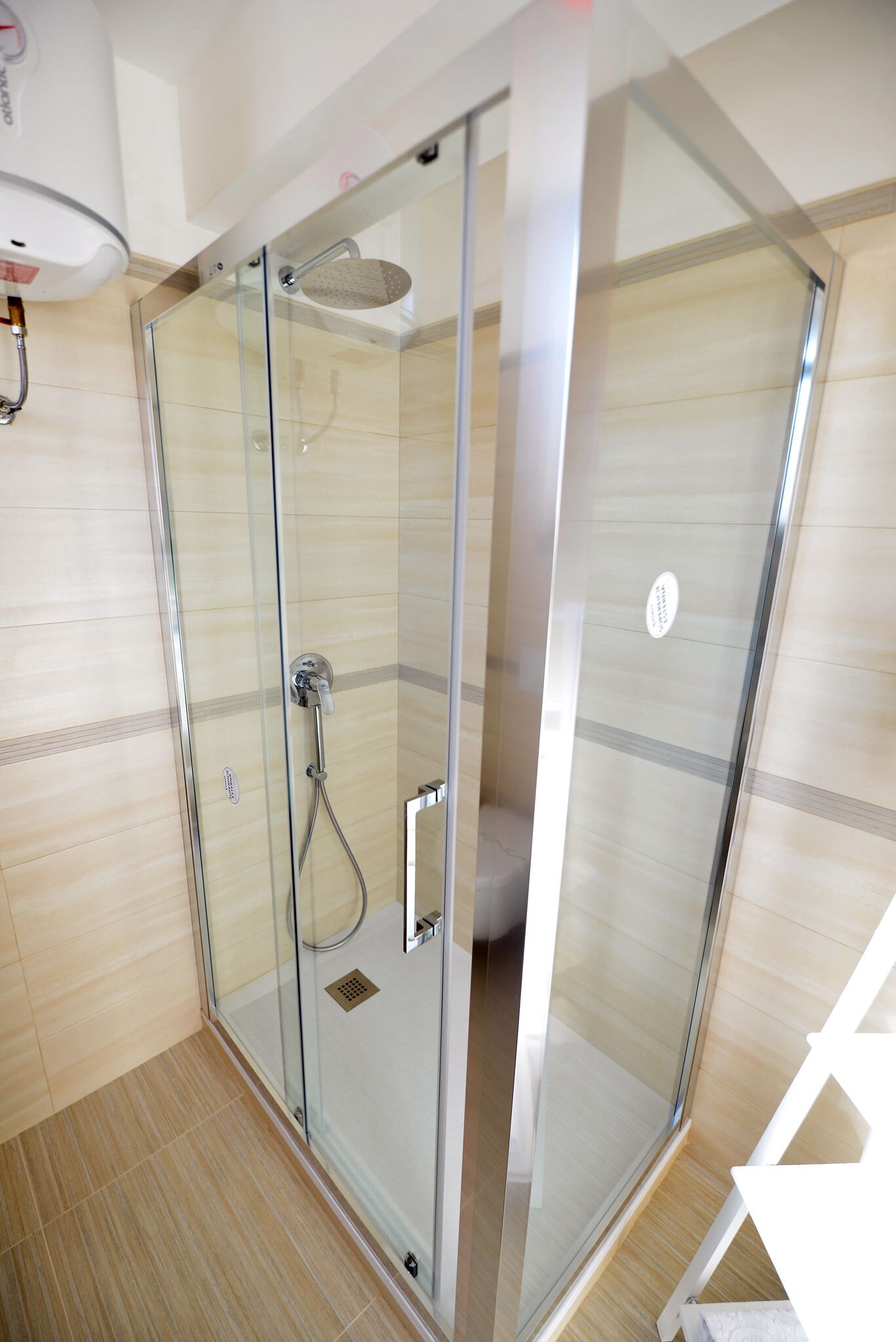 Een moderne douchecabine met glazen deur, een handdouche en een wandmengkraan.