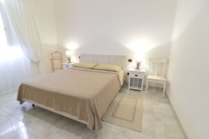 Um quarto com uma cama, mesas de cabeceira, uma cadeira e um criado-mudo.