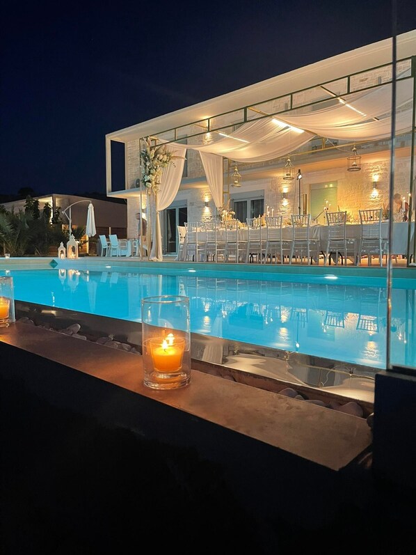 A poolside area with a dining setup, including tables and chairs, and a candle on the bar counter.