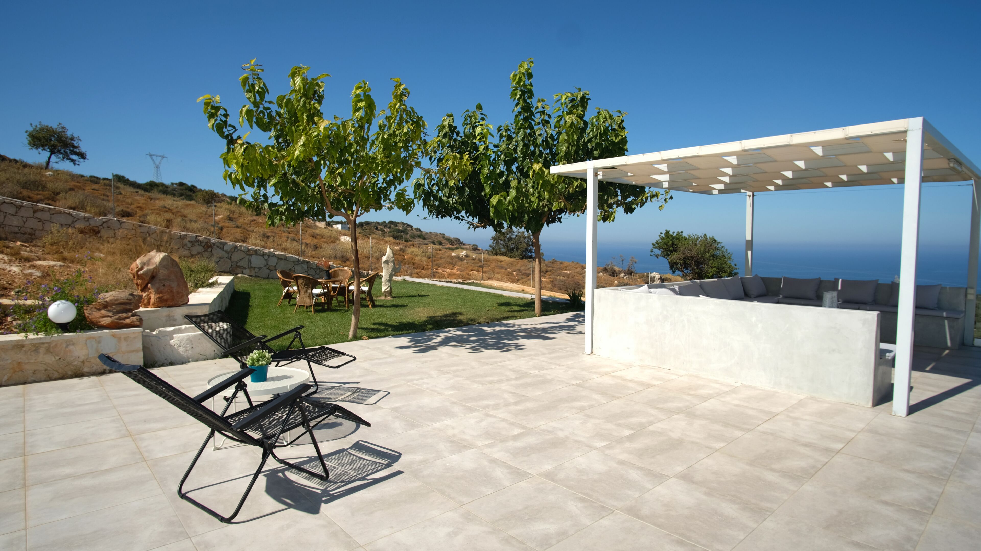 Een buitenpatio met een pergola, een zithoek en uitzicht op zee.
