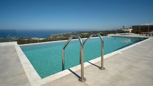 Une piscine à l’eau d’un bleu cristallin, entourée d’une terrasse carrelée et offrant une vue panoramique sur la mer et le paysage environnant.