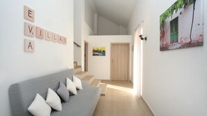 Un intérieur moderne avec un canapé gris, un escalier et un mur orné de carreaux formant le mot « EVILLAS ».