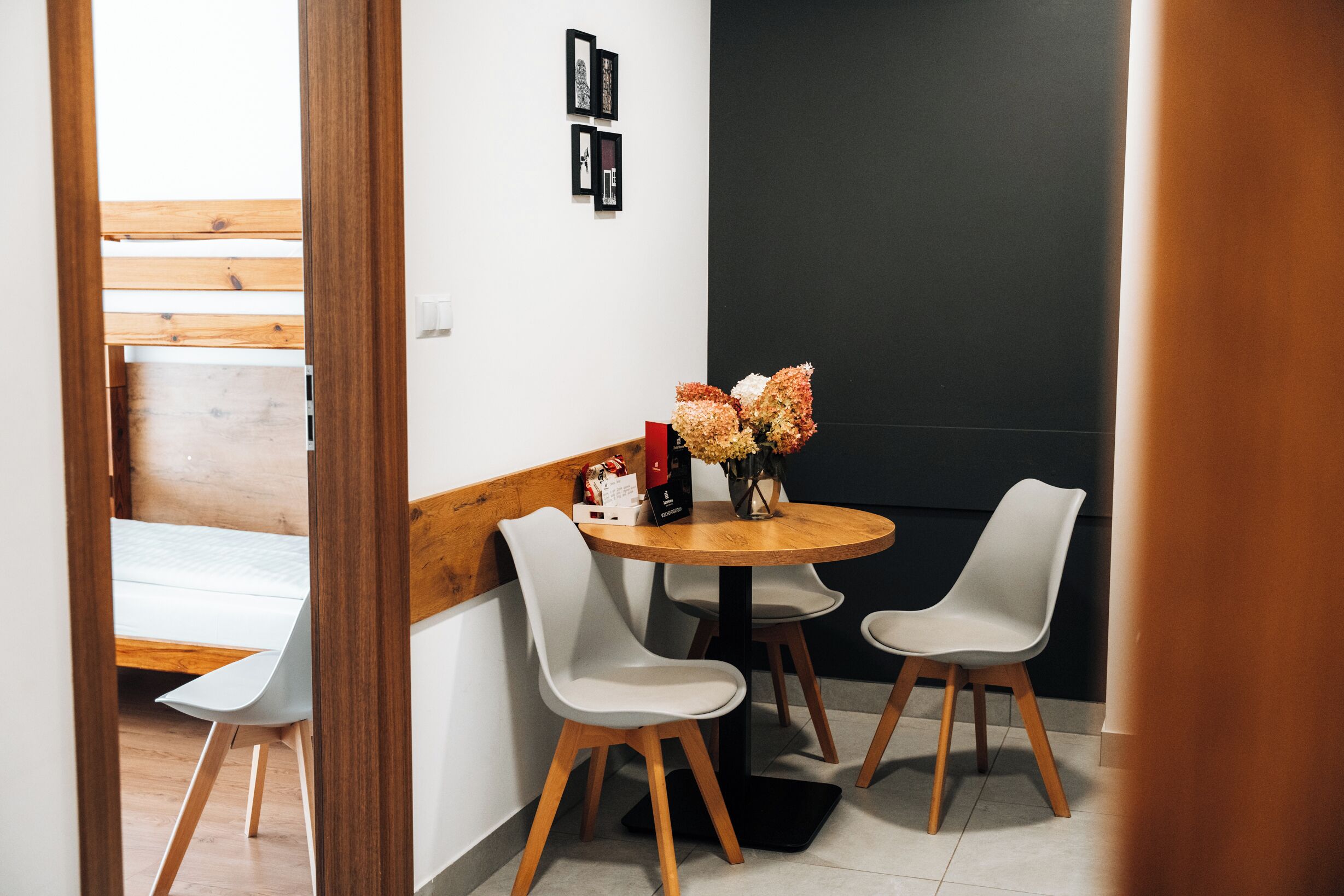A modern dining area with a round wooden table, two white chairs, and a vase of flowers.