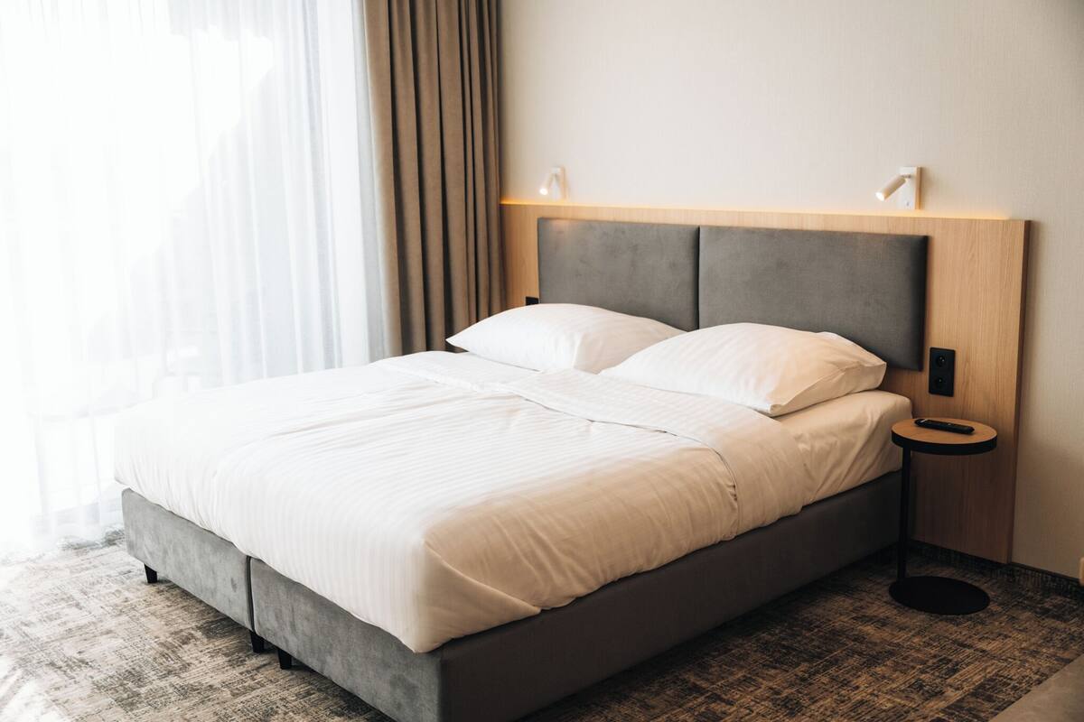 A modern hotel room with a large bed, a bedside table, and a wall-mounted light fixture.