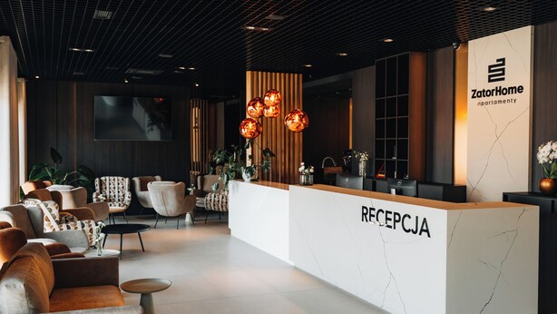 A modern reception area with a marble reception desk labeled "RECEPCJA" and "ZatorHome apartmenty" sign. - ZatorHome apartamenty (Zator)