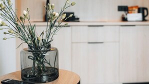 A modern kitchen with wooden cabinets, a glass vase with flowers on a round table, and a remote control on the table. - ZatorHome apartamenty (Zator)