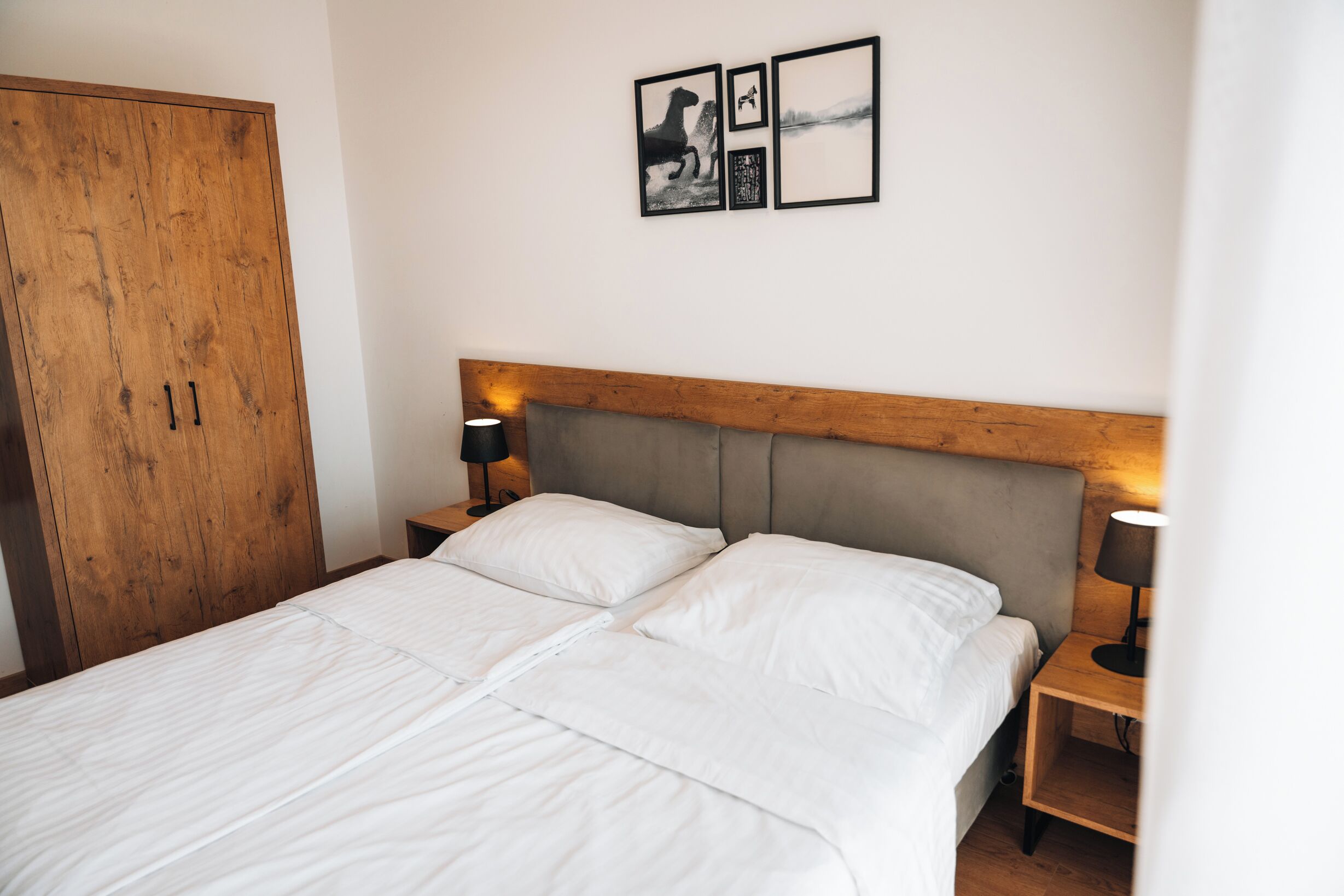 Un dormitorio con cabecera de madera, una cama con ropa blanca, dos mesitas de noche con lámparas y un armario de madera.