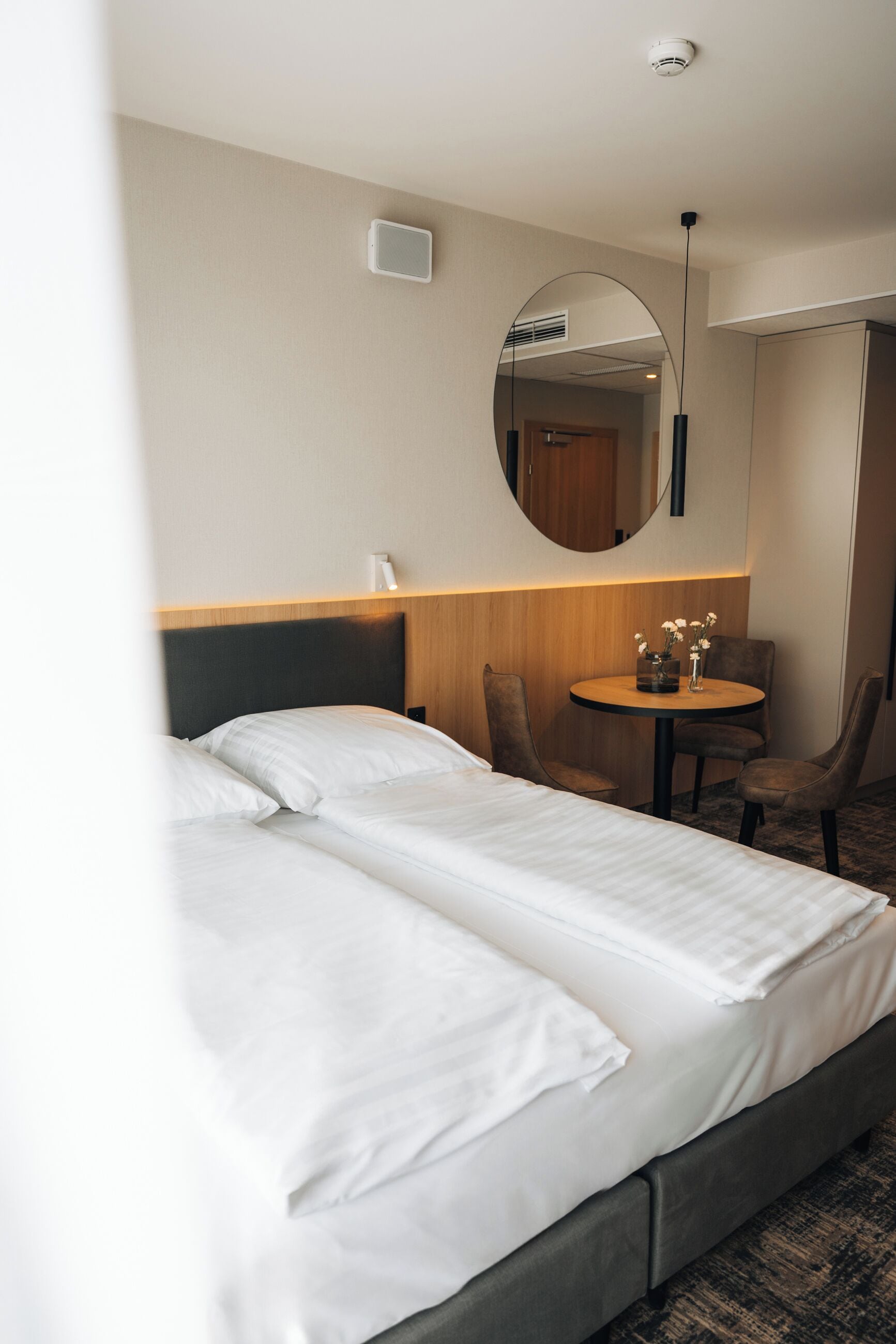 Een hotelkamer met een bed, een ronde tafel met stoelen, een spiegel en een plafondlamp.