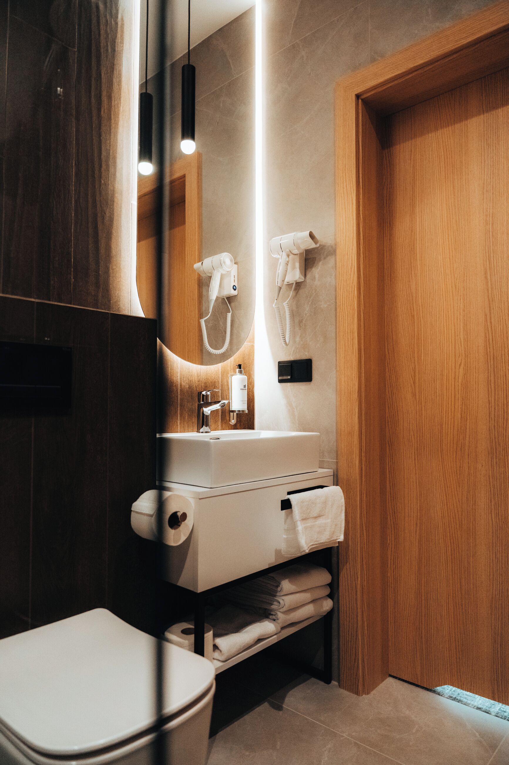 A modern bathroom with a wooden vanity, a mirror, a towel rack, and a toilet.