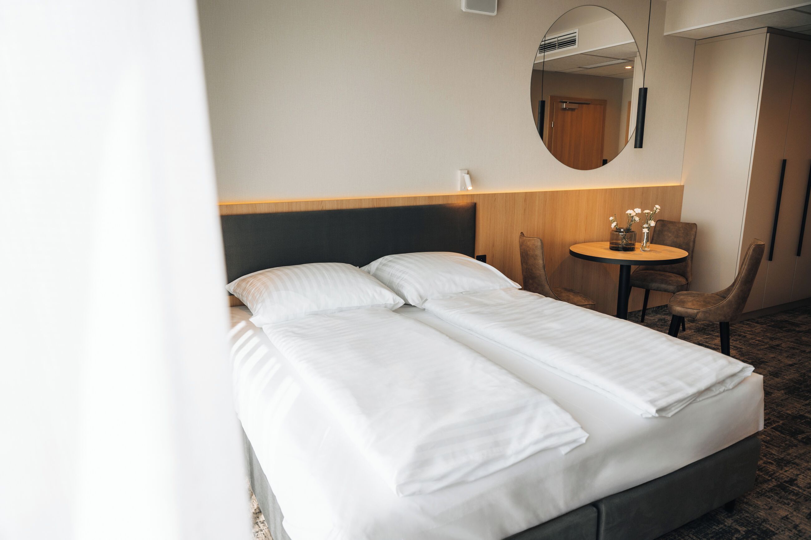 Habitación de hotel con cama doble, una mesa redonda con sillas, un espejo y un cabecero de madera.