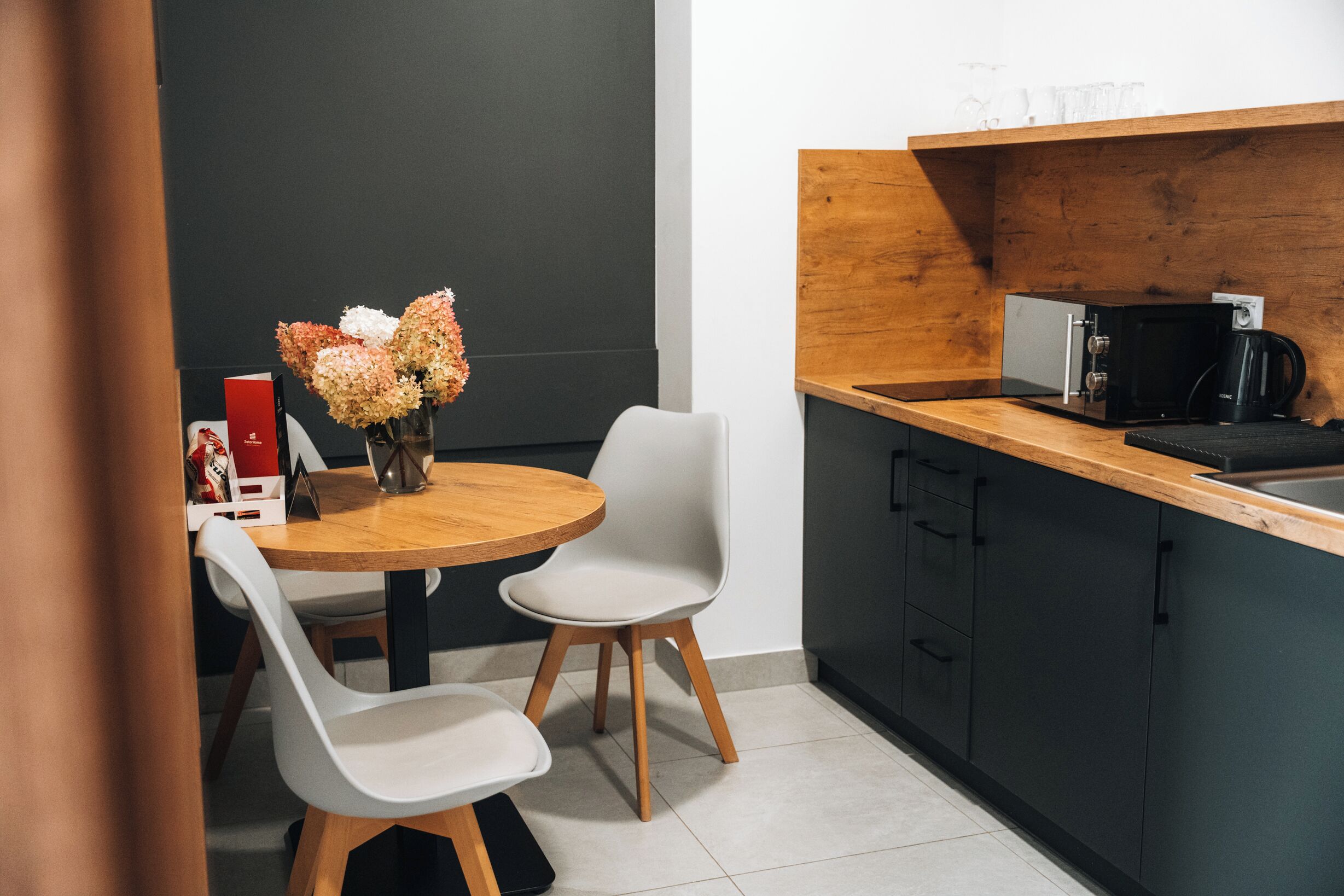 A modern kitchen with a wooden countertop, a coffee machine, and a vase of flowers on the table.