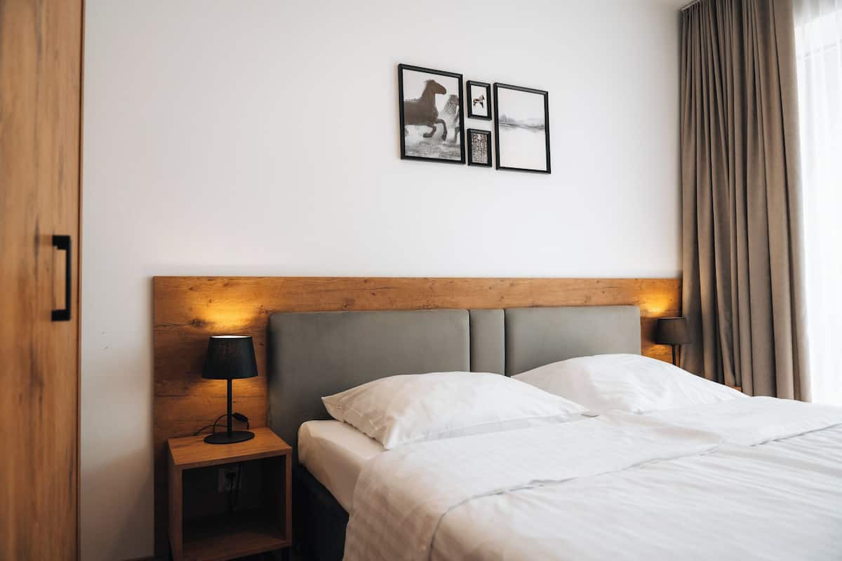 A hotel room with a wooden headboard, a bed with white linens, a nightstand with a lamp, and three framed pictures on the wall.