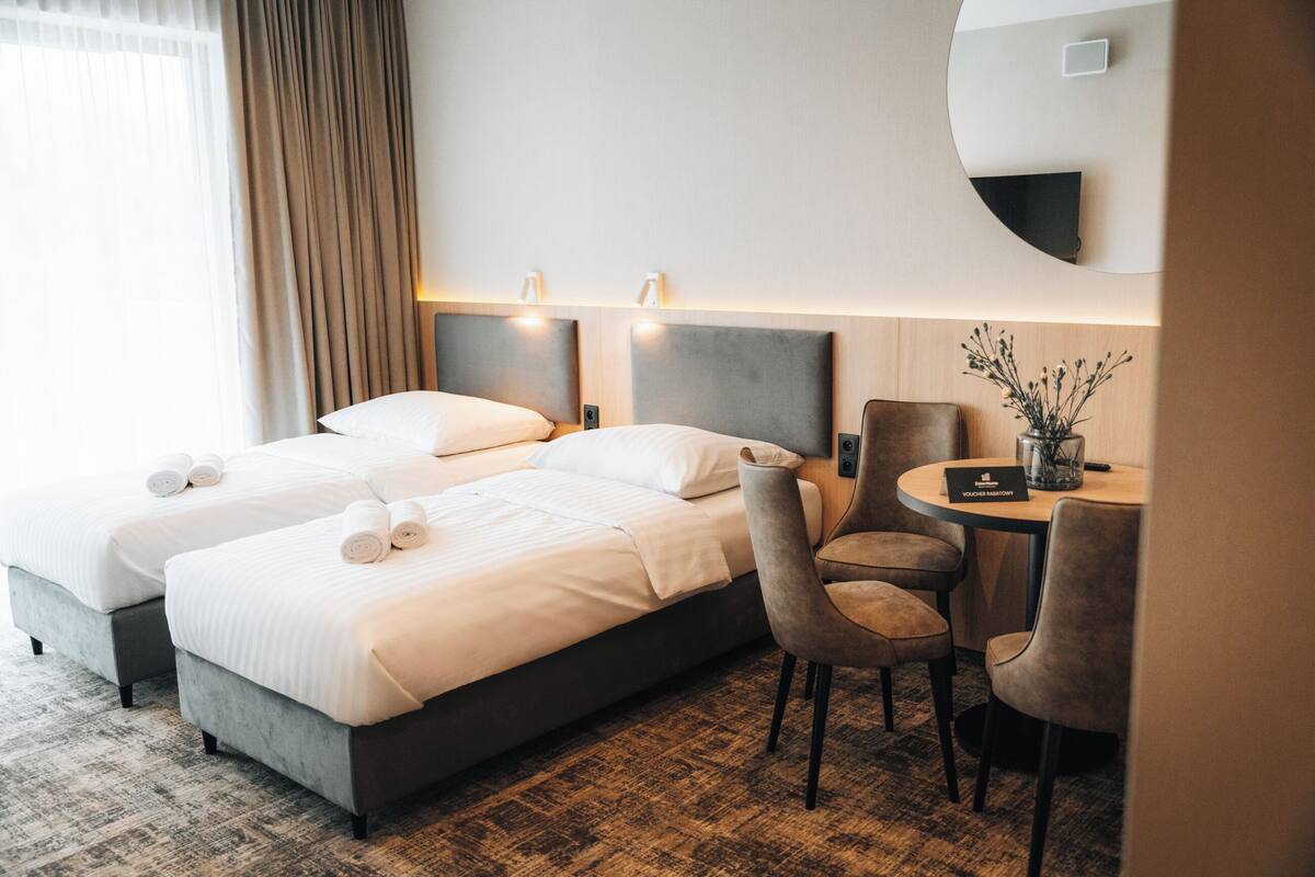 A hotel room with two beds, a round table with a vase, and a chair.