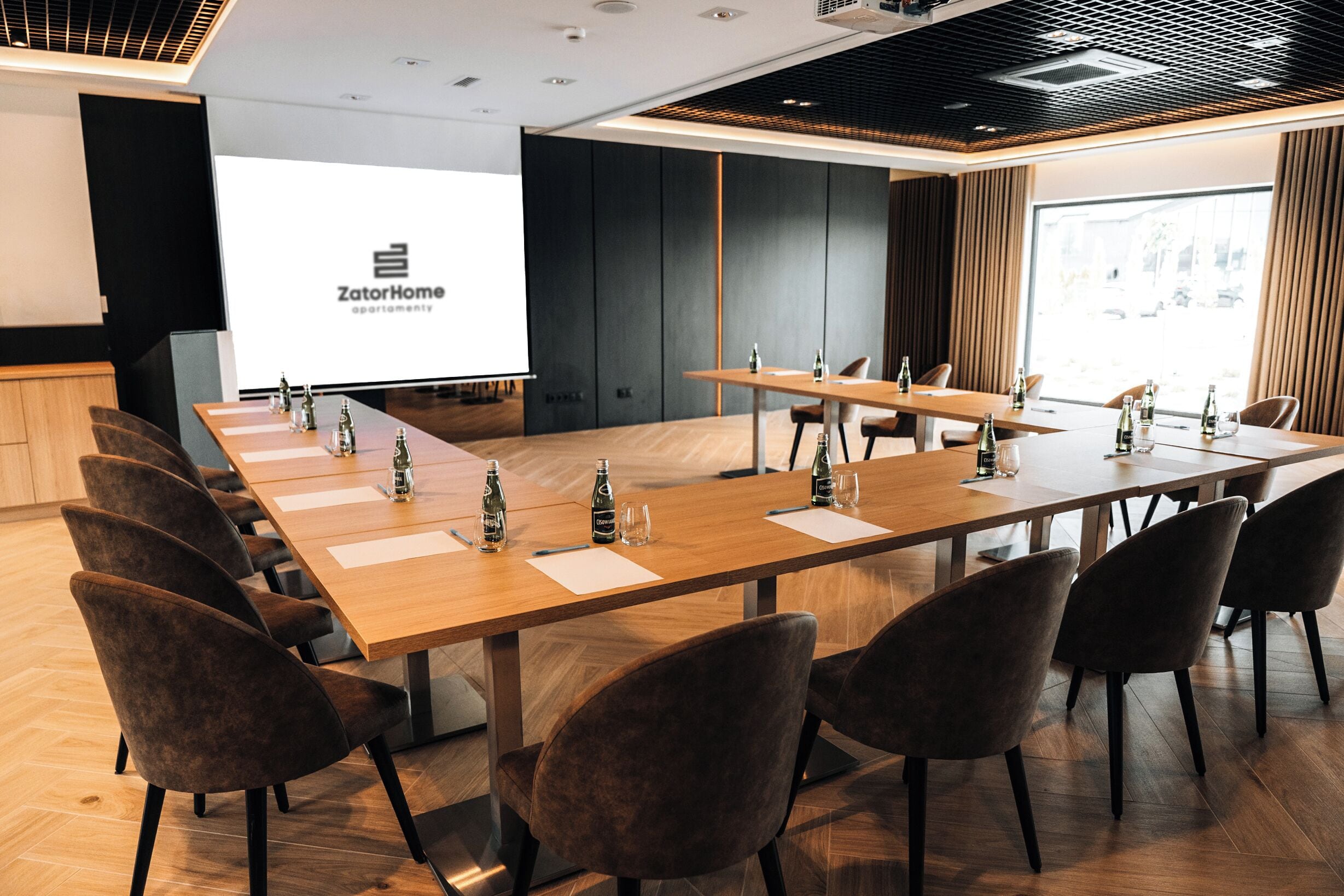 A conference room with a long table, chairs, and a projector screen displaying 'ZatorHome apartment'.