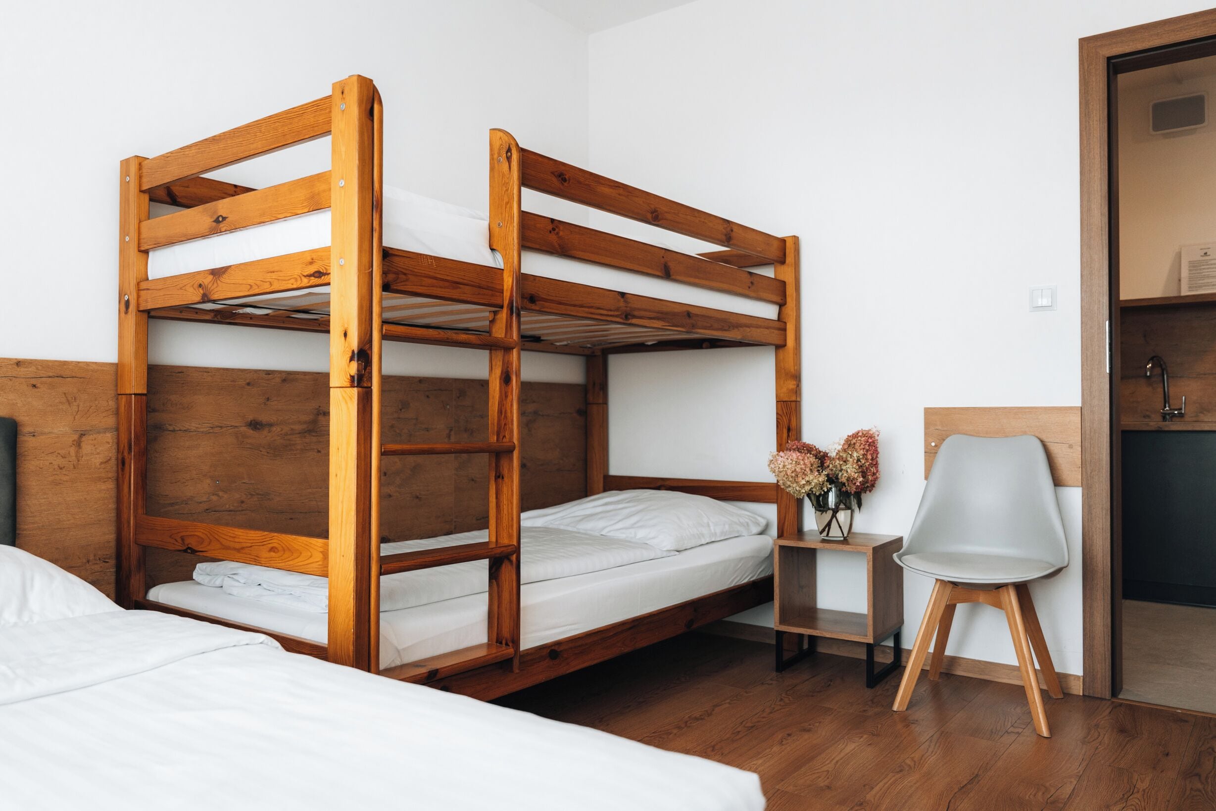 A bunk bed room with a wooden headboard, a small table with flowers, and a chair.
