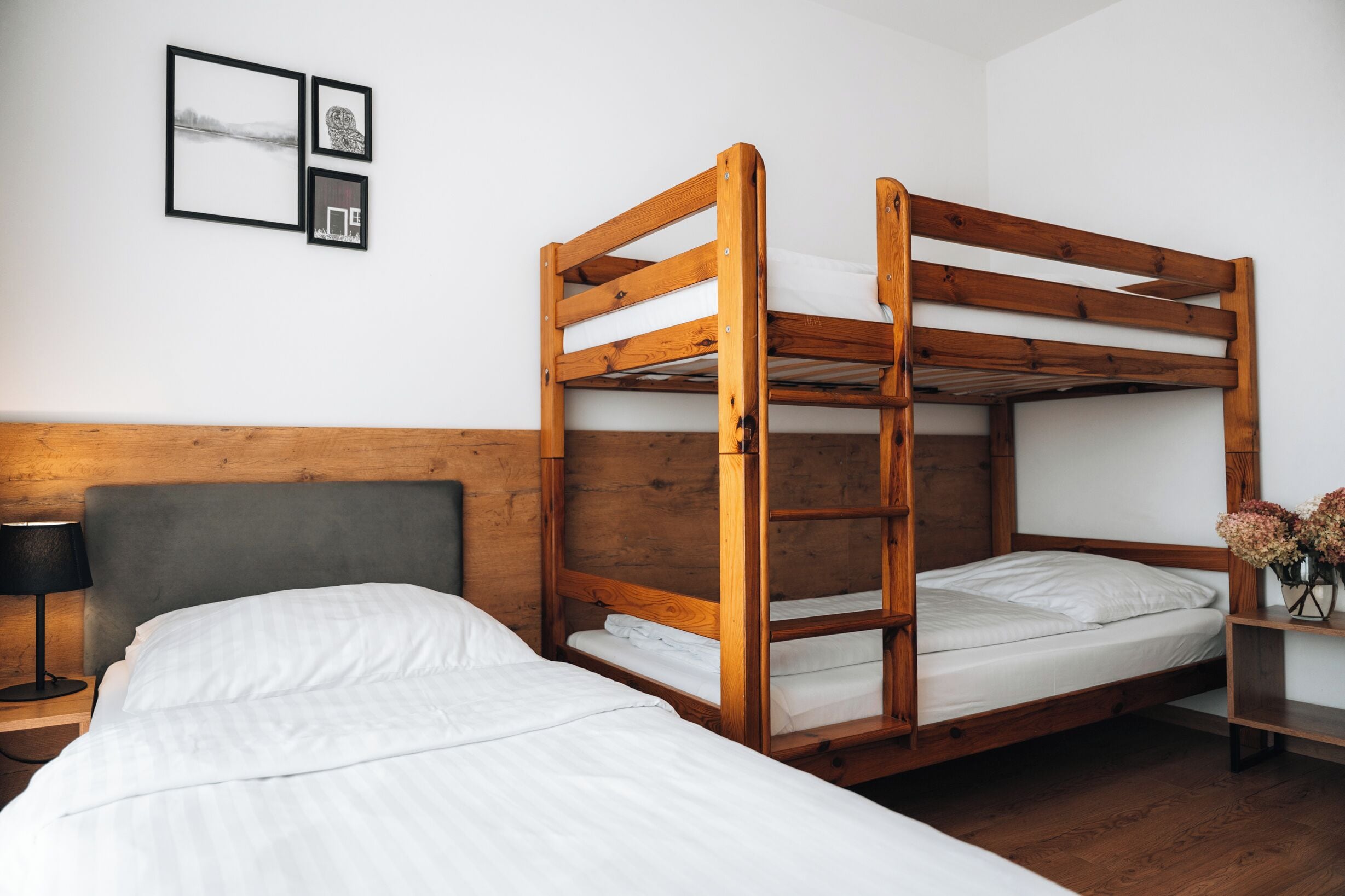A bunk bed room with a wooden headboard, a bedside table with a lamp, and framed pictures on the wall.