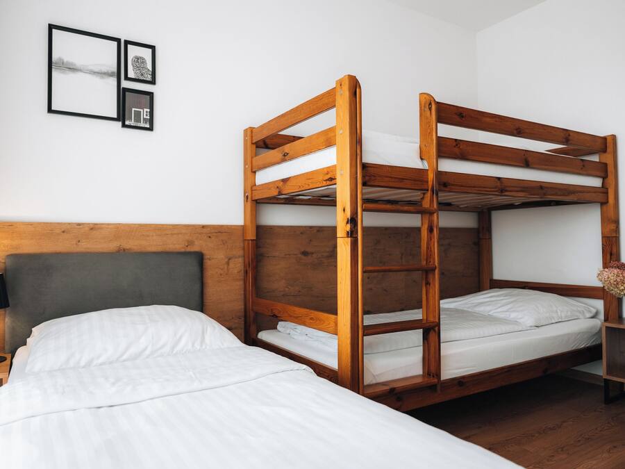 A bunk bed room with a wooden headboard, a bedside table with a lamp, and framed pictures on the wall.