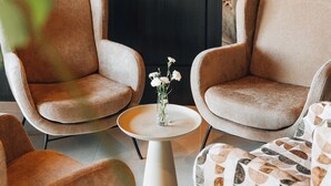 A modern living room with two armchairs, a small round table with a vase of flowers, and a television mounted on the wall. - ZatorHome apartamenty (Zator)
