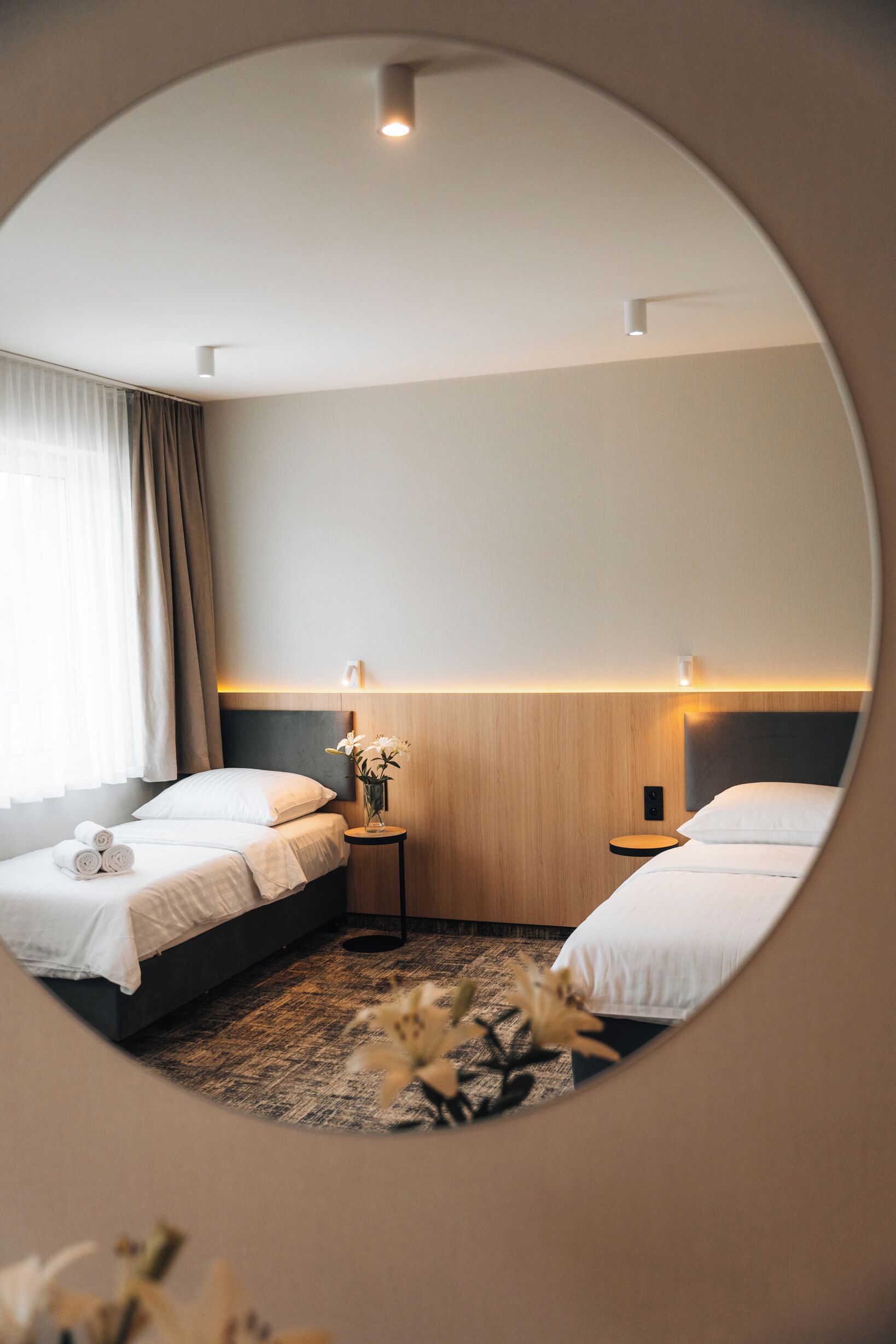 Une chambre d’hôtel avec deux lits, une petite table de chevet ornée d’un vase de fleurs et une tête de lit dotée d’un éclairage intégré.