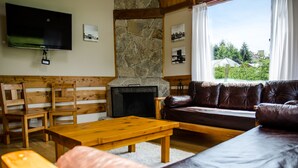 A living room with a stone fireplace, wooden furniture, a leather sofa, and a TV mounted on the wall. - MOUNTAIN CABIN DREAM (San Carlos de Bariloche)