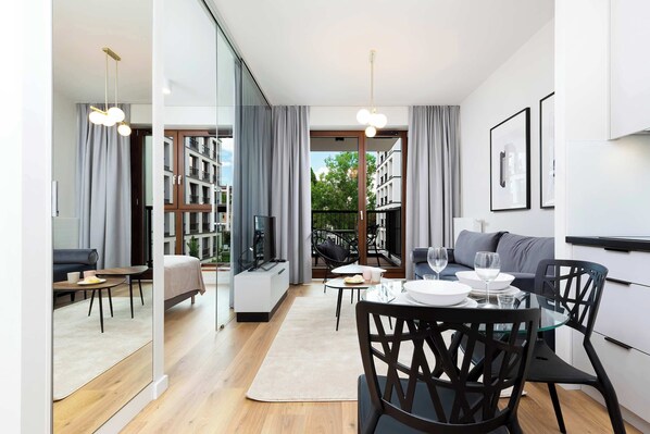 A bright, spacious living room with a sofa, coffee table, and a dining area near large balcony windows.