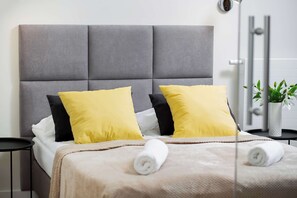 A comfortable bed with fresh white linens and yellow pillows placed near large windows.