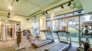 A gym with treadmills, weight machines, and a large window offering a view of buildings and greenery. - Jurmala Park House (Jurmala)