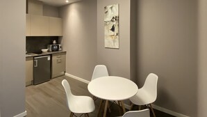 A modern dining area with a round table and four chairs, a kitchen in the background, and a ceiling light fixture. - Jurmala Park House (Jurmala)