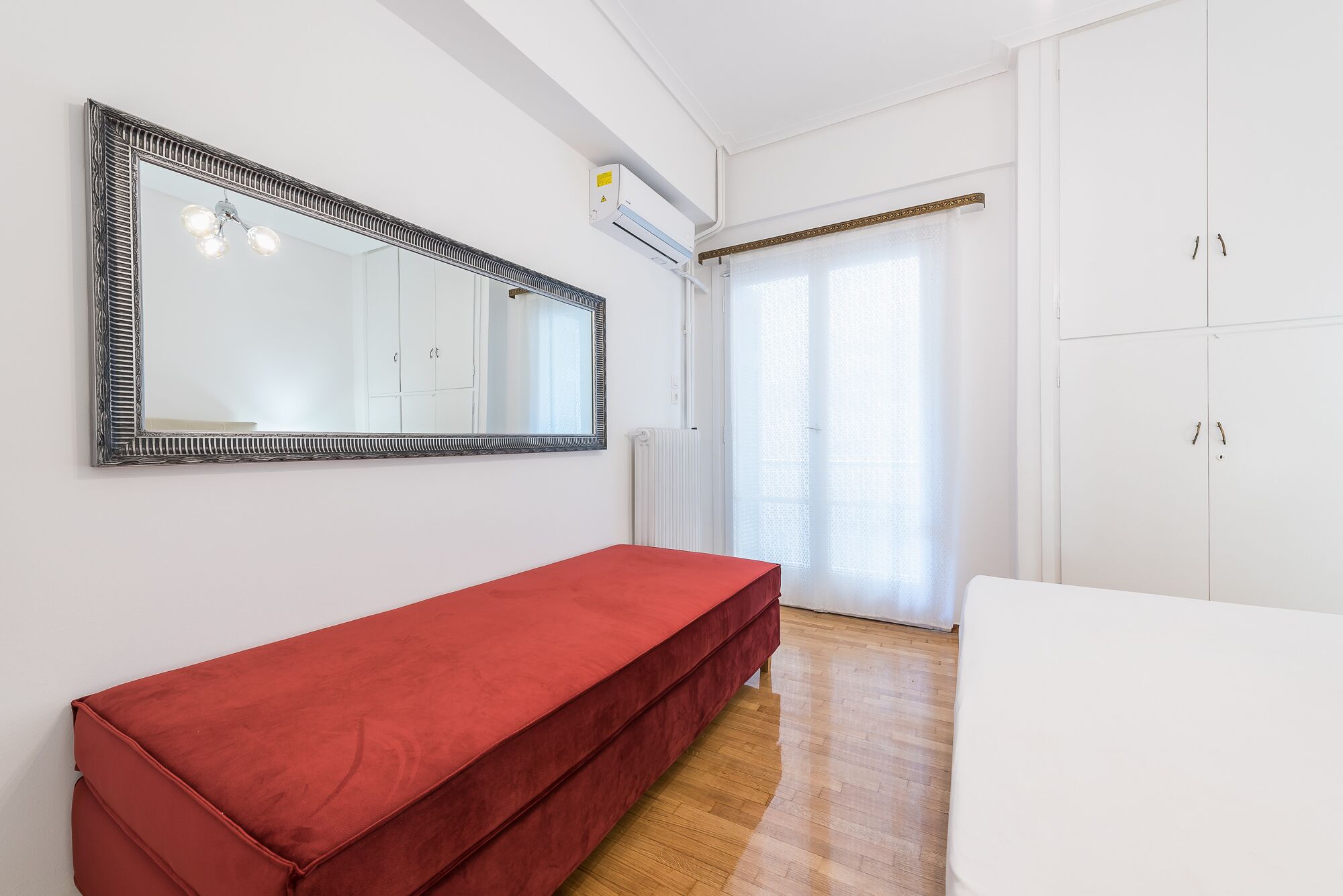 A room with a red bench, a large mirror, white cabinets, and a radiator.