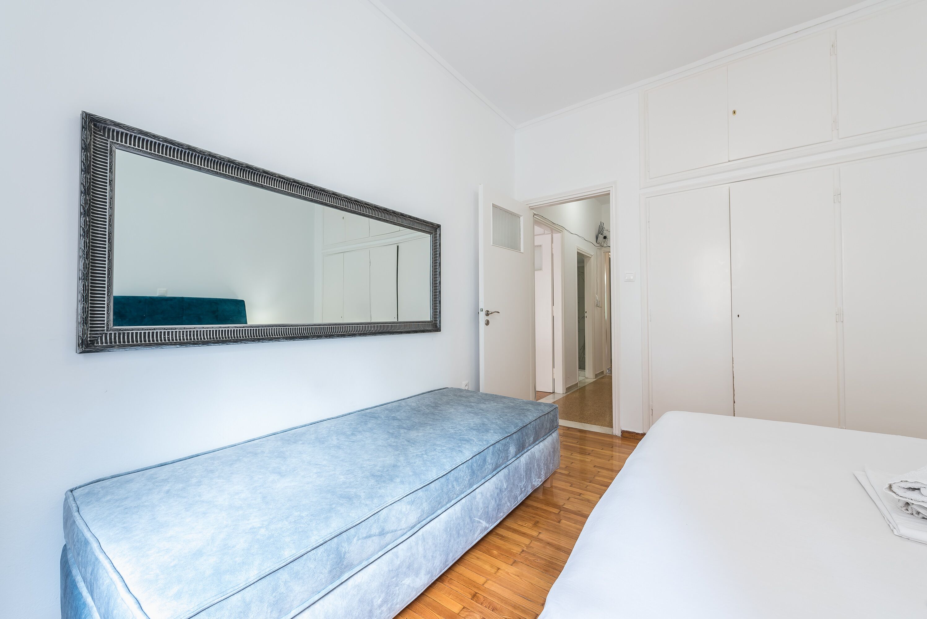 A bedroom with a large bed, a bench, a wardrobe, and a mirror.