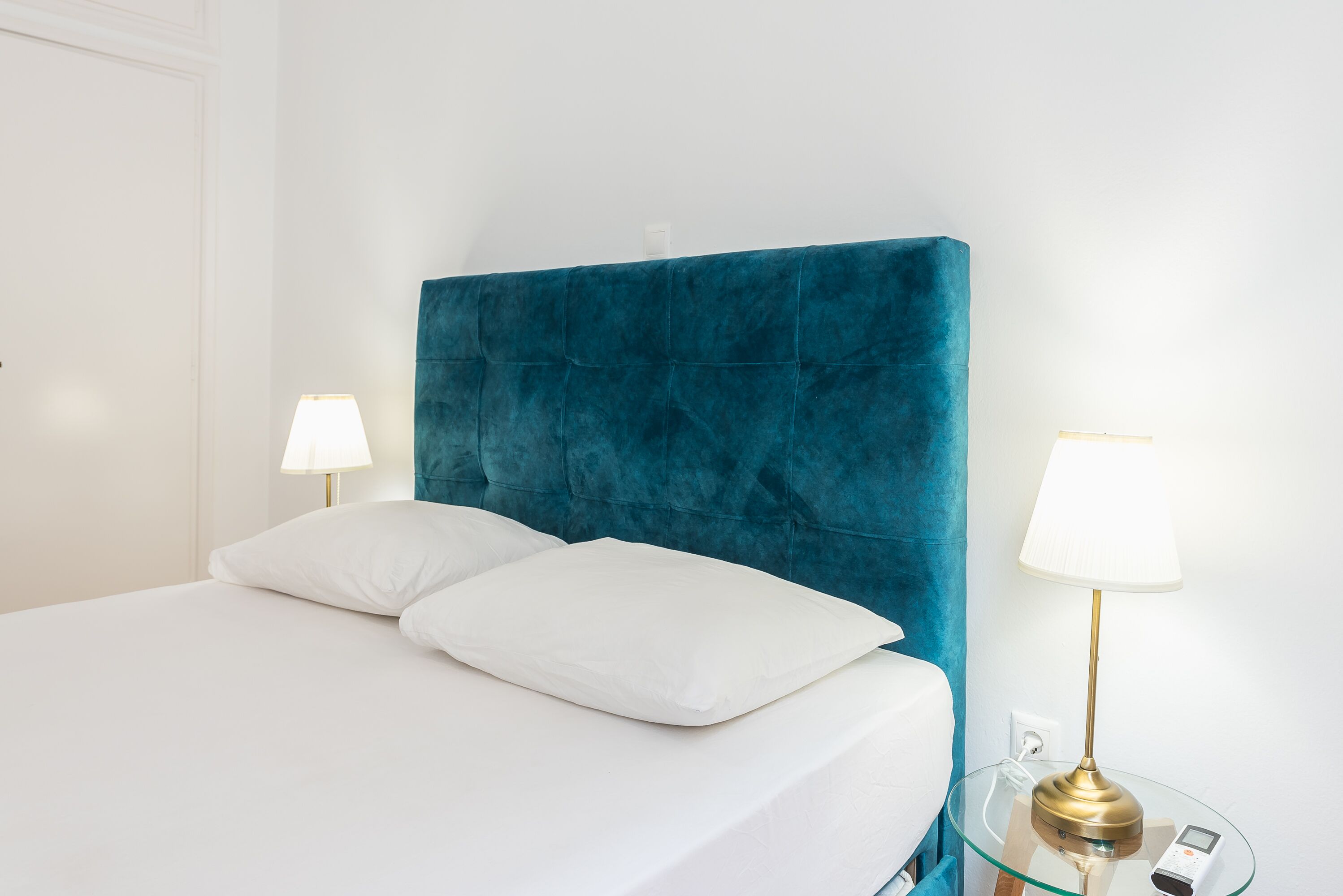 A bed with white bedding, a teal upholstered headboard, and two bedside lamps with white shades.