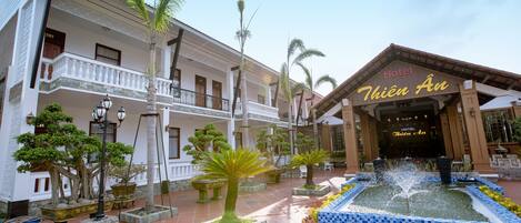 Un hotel de estilo arquitectónico tradicional, con un patio central que tiene una fuente, plantas en macetas y un camino empedrado.
