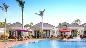 A swimming pool with lounge chairs and umbrellas, surrounded by palm trees and a building with a tiled roof. - Thien An Hotel (Can Tho)
