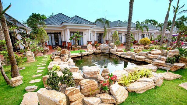 A landscaped garden with a pond, large rocks, and palm trees. - Thien An Hotel (Can Tho)