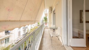 A balcony with a white chair and table, a white door, and a view of neighboring buildings. - Victoria Supreme Suite (Athens)