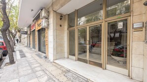 A building facade with large glass windows, a tiled entrance, and a metal fence. - Victoria Supreme Suite (Athens)