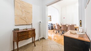 A hallway leading to a dining area with a wooden table and chairs, a large map on the wall, and a vintage-style dresser with drawers. - Victoria Supreme Suite (Athens)