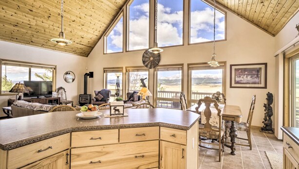 A spacious kitchen with a large island, wooden cabinetry, and a dining area with a wooden table and chairs. - Quiet Fairplay Cabin w/ Rocky Mountain Views! (Fairplay)
