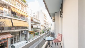 Un balcone con un tavolo e una sedia, affaccia su una strada con edifici e negozi.
