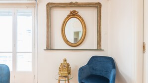 A room with a blue chair, a small table with a clock, and a large mirror on the wall. - Athens Empire Paradise Apartment (Athens)