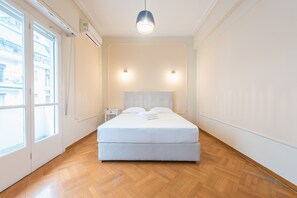 A bedroom with a large bed, wooden flooring, a window, and two wall-mounted lights. - Athens Empire Paradise Apartment (Athens)
