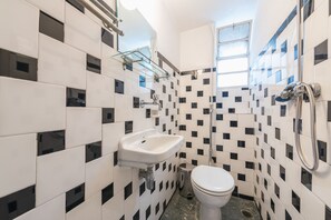 A bathroom with a white sink, toilet, and shower. The walls are tiled with a black and white pattern. - Athens Empire Paradise Apartment (Athens)