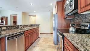 A kitchen with granite countertops, stainless steel appliances, wooden cabinets, and a tiled floor.