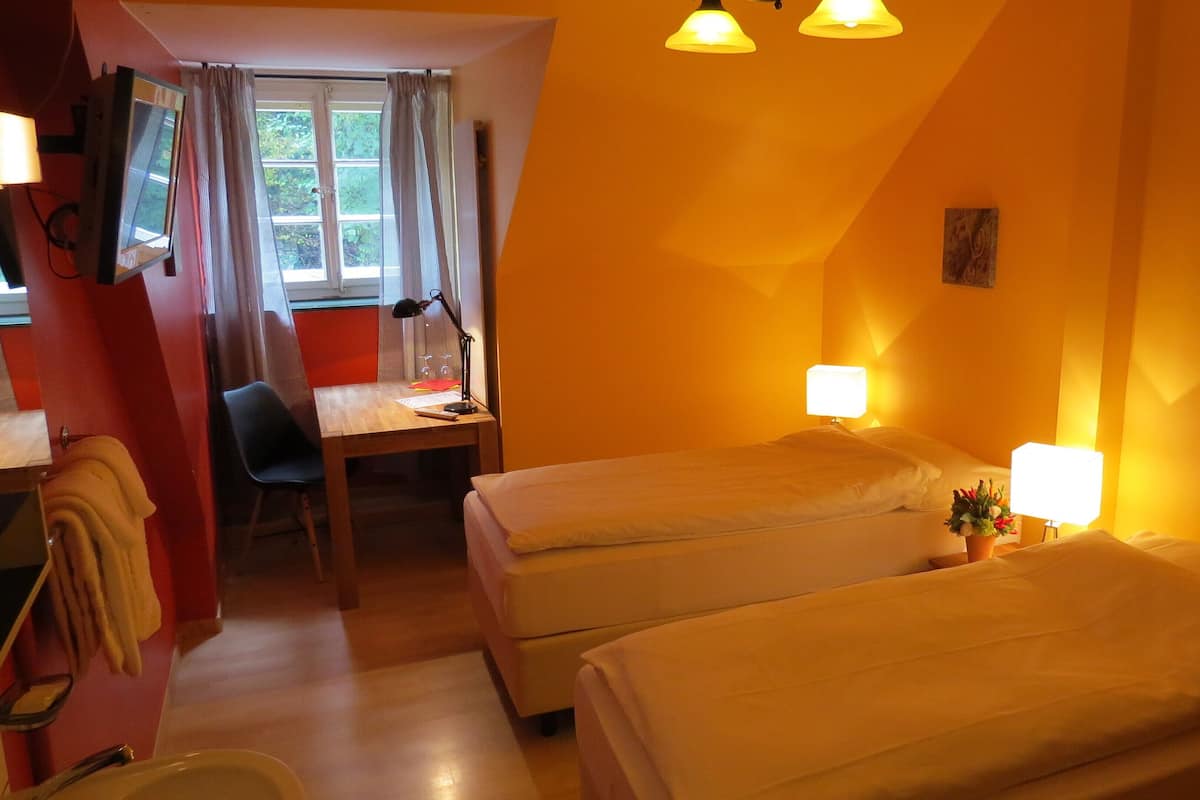 Habitación de hotel con dos camas, un escritorio con silla, televisión y ventana con cortinas.