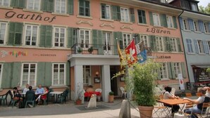 Un edificio con un letrero que dice "Gastrof" y "z. Baron", indicando un restaurante o bar. Cuenta con espacios de esparcimiento al aire libre con mesas y sillas.