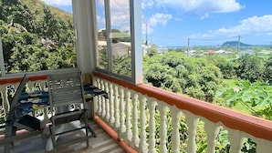A balcony with a view of a lush green landscape, a metal chair, and a railing. - Auberge K-Wan Hostel (Deshaies)